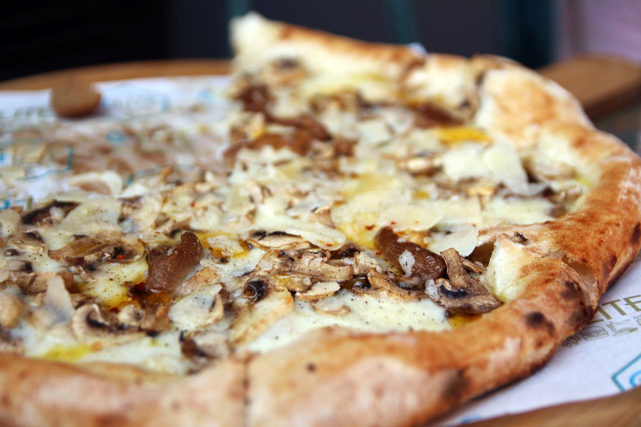 Mouthwatering close-up of a mushroom and cheese pizza slice with scattered toppings.